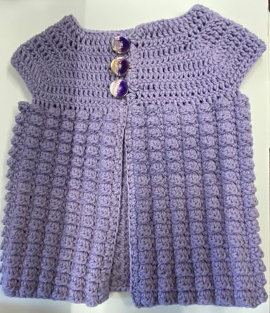 Purple crocheted garment with a textured design and three decorative buttons.